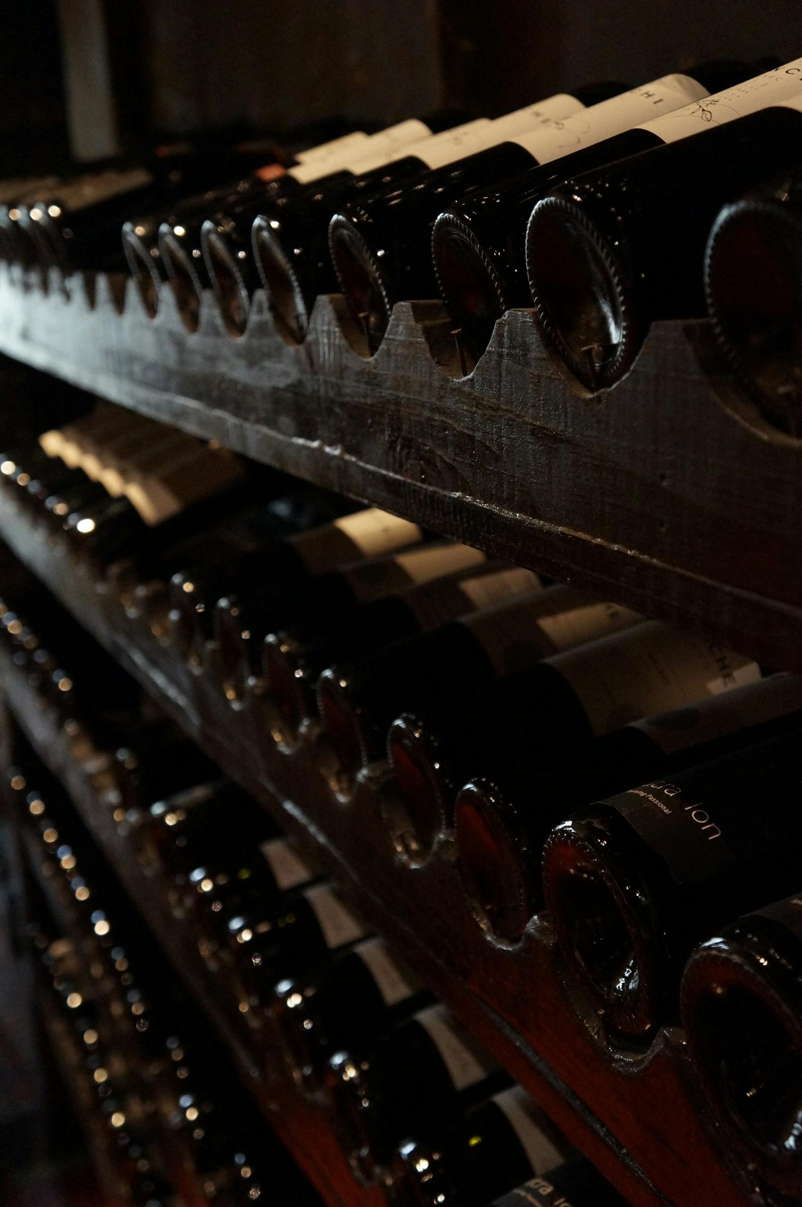 A dimly lit wine cellar showcasing rows of wine bottles on rustic wooden shelves, creating a classic and elegant atmosphere.